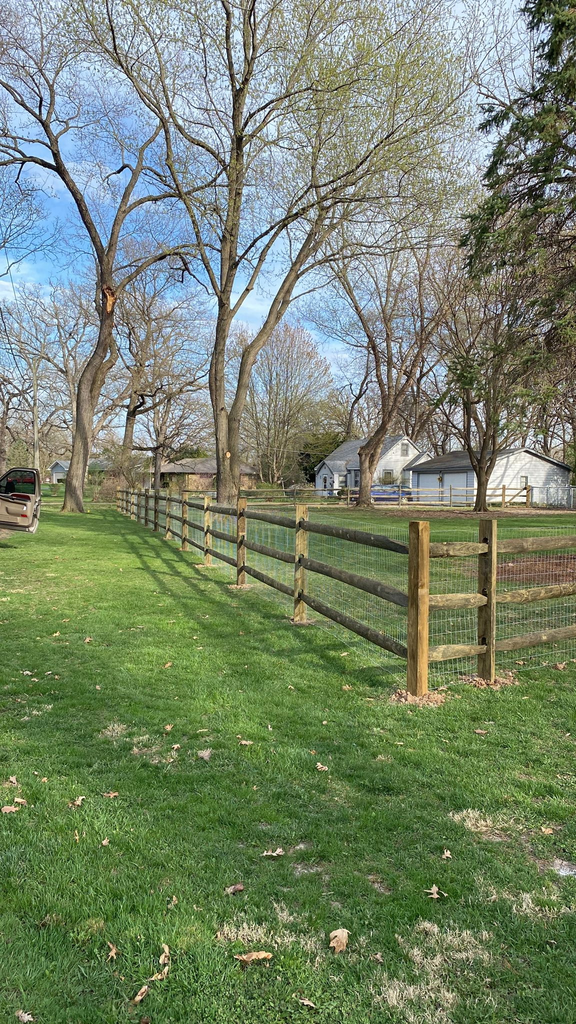 Split rail wood fence beside a lawn and mature trees.