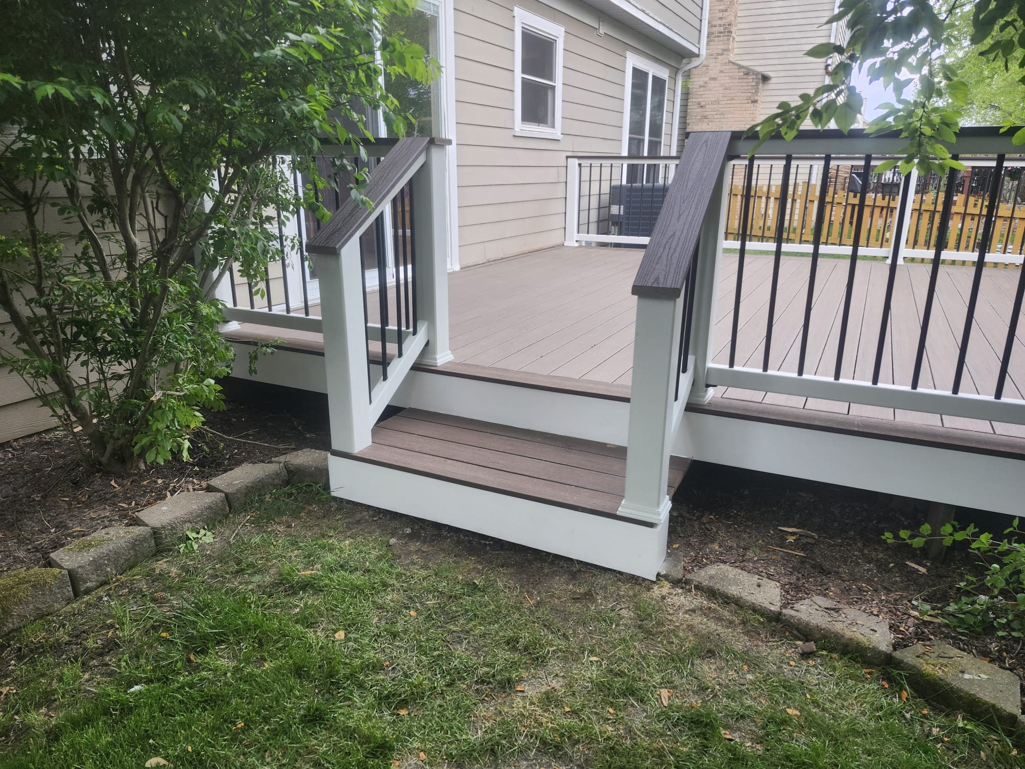 Deck steps with light posts and dark railing balusters beside a house.
