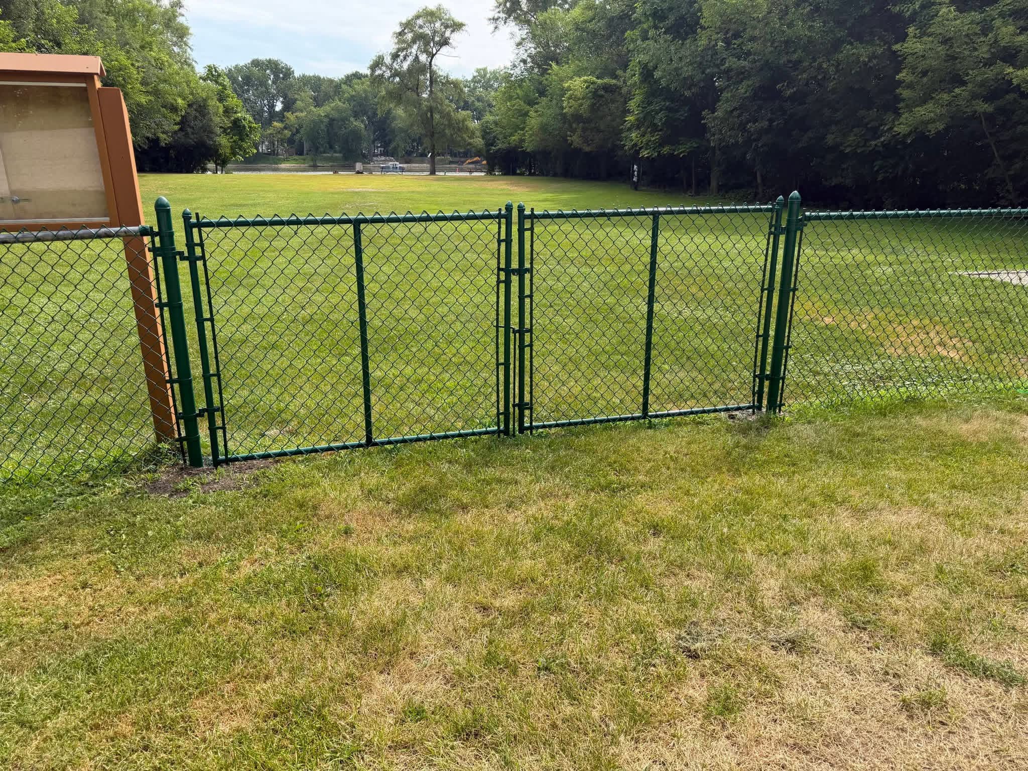 Black chain link double gate opening onto a lawn.